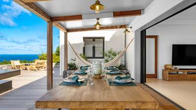 Elegant alfresco dining on the covered terrace featuring a long wooden table, relaxing hammock, and breathtaking ocean views.