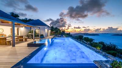 Magnificent heated swimming pool and wooden terrace offering panoramic ocean views at dusk in this luxury St-Barths villa.