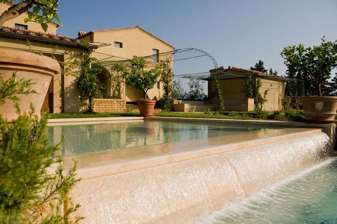 Elegant infinity pool with a cascading waterfall at luxury Villa Marchesa, featuring rustic Tuscan architecture and views.