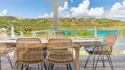 Elegant outdoor dining area on the covered terrace featuring a live-edge wood table and panoramic views of Marigot Bay.