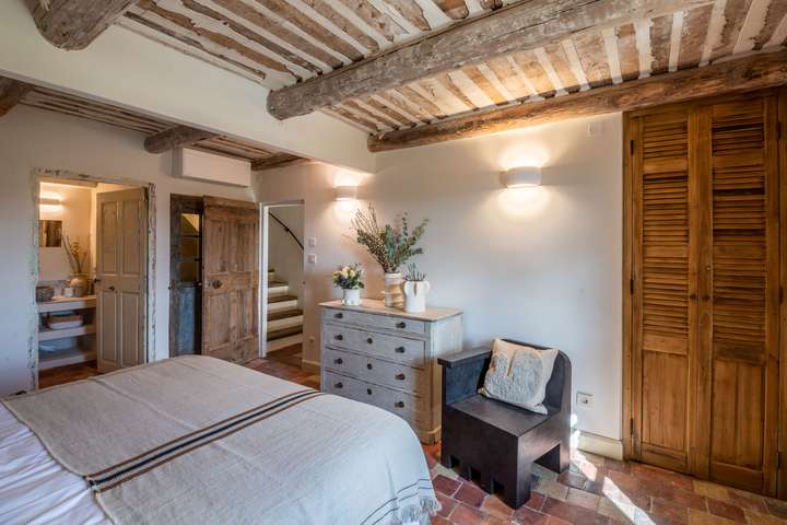 Luxury air-conditioned bedroom with reclaimed wood beams, terracotta tiles, and a sleek en-suite bathroom in Gordes.