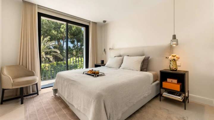 Elegant guest bedroom suite with neutral tones, plush bedding, and sliding doors opening to the lush garden terrace.