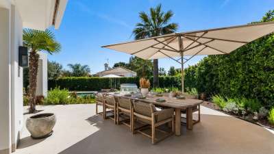 Elegant alfresco dining area at Monteros Sands, featuring a rustic wooden table, woven chairs, and a large sun umbrella.