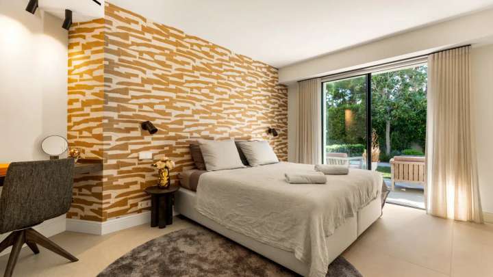 Luxury guest bedroom suite at Monteros Sands with a textured accent wall and direct access to the lush garden terrace.