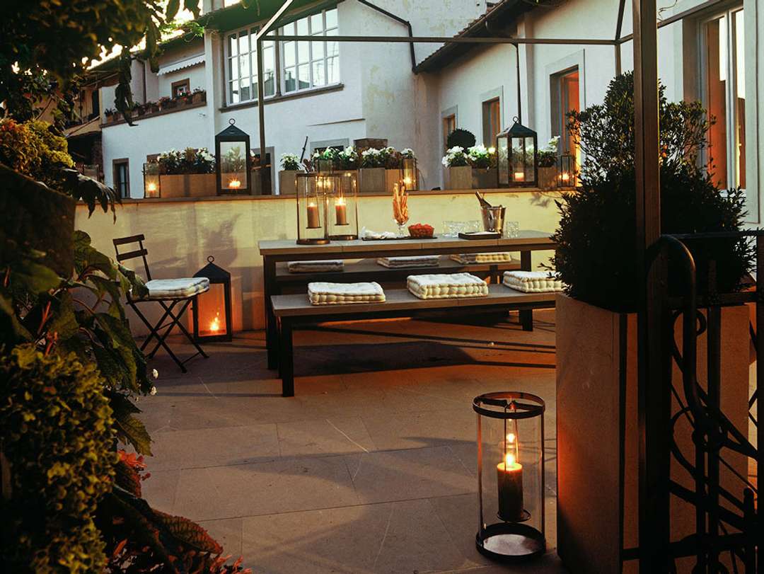Elegant private roof terrace in Florence featuring a pergola-shaded dining area illuminated by romantic candlelit lanterns.