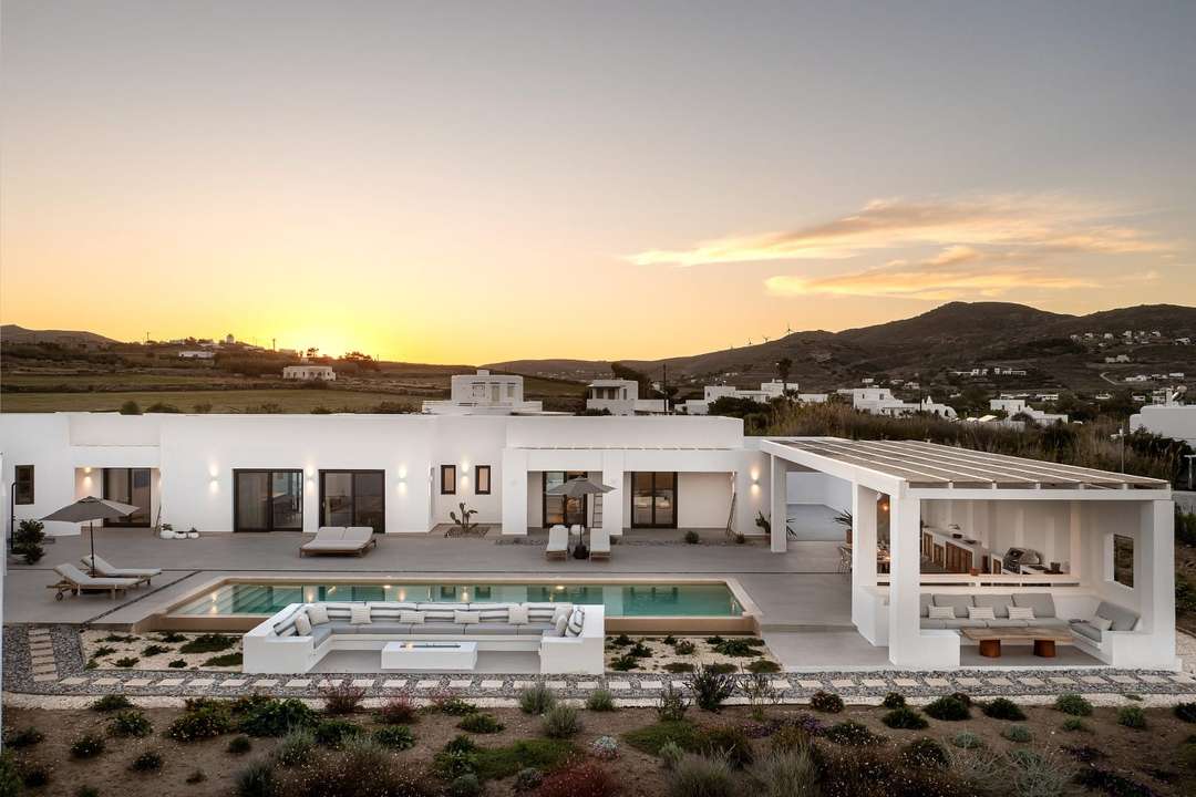 Contemporary Cycladic villa at sunset featuring a large private pool, sunken lounge, and elegant outdoor dining in Paros.