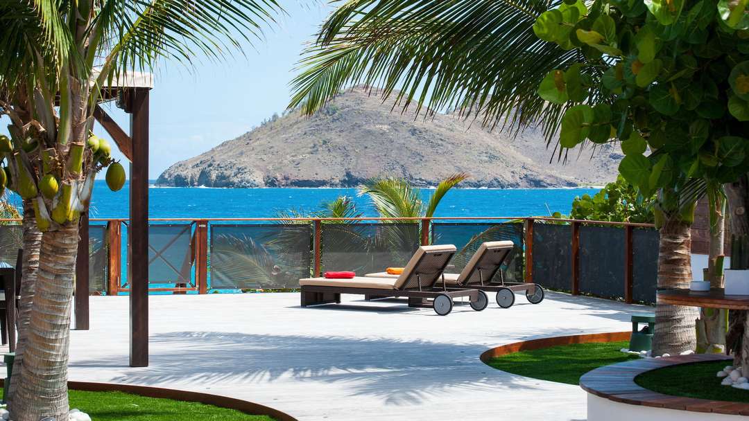 Relax on plush sun loungers on Villa Micela's expansive wooden deck, offering breathtaking ocean views of Flamands Beach.