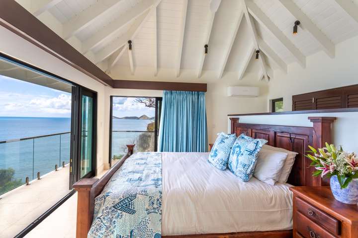 Elegant bedroom suite with a hardwood king bed, vaulted ceilings, and expansive glass doors framing breathtaking sea views.