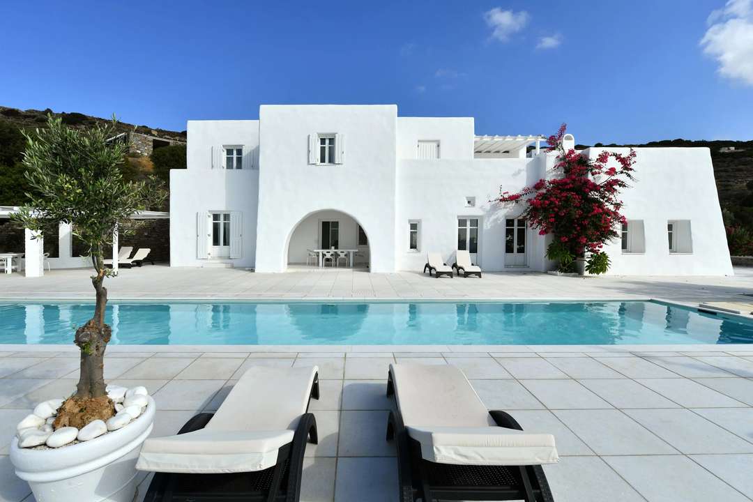 Striking white luxury villa in Paros featuring a private pool, sun loungers, and minimalist architecture under a blue sky.