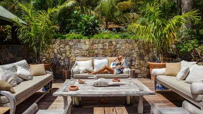 Elegant outdoor lounge area with plush sofas, a rustic wooden coffee table, and tropical garden views at luxury Villa Nahma.