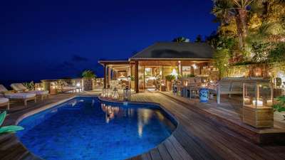 Breathtaking night view of the luxury villa's wooden terrace, heated pool, and elegant outdoor lounge overlooking the ocean.