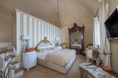 Elegant bedroom at Villa Nume with a gold ornate bed, striped walls, antique wooden wardrobe, and luxury furnishings.