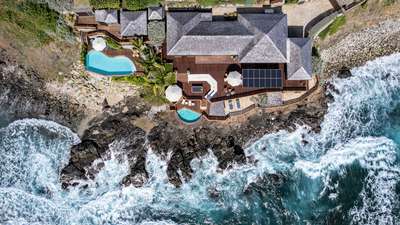 Top-down aerial of a St. Barths luxury villa with a private pool, jacuzzi, and wooden terraces on a dramatic rocky cliff.
