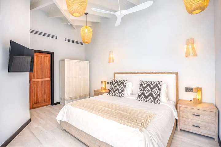 Bright king bedroom at Ocean 19 with high raftered ceilings, woven pendant lights, smart TV, and natural wood accents.
