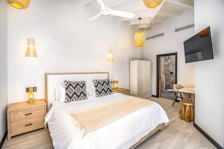 Airy king bedroom at Ocean 19 offering high raftered ceilings, woven lighting, smart TV, and a luxurious en-suite bathroom.
