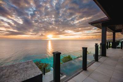 Expansive outdoor terrace at Ocean One villa featuring glass railings and offering breathtaking panoramic sunset ocean views.