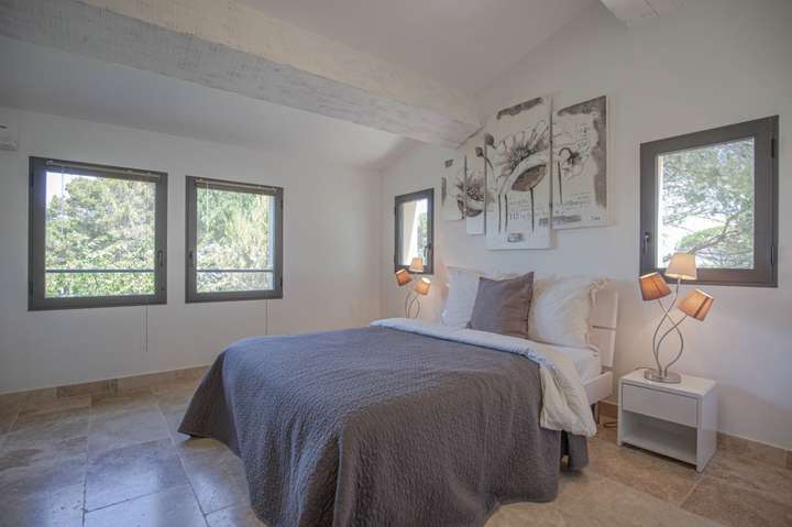 Charming upstairs villa bedroom with exposed wooden beams, a plush queen bed, and bright windows offering nature views.