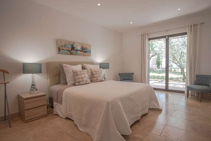 Luxurious ground-floor villa bedroom with a plush bed, stone floors, and glass doors opening to the landscaped garden.
