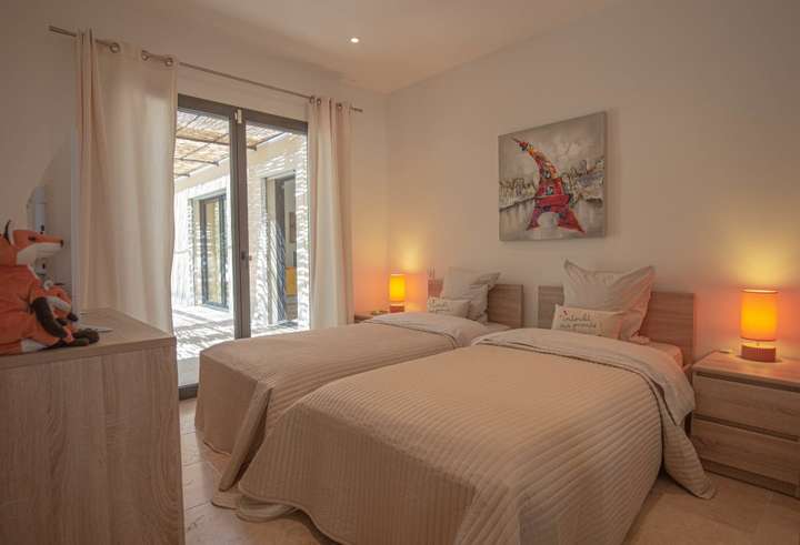 Luxury villa twin bedroom featuring contemporary decor, natural stone floors, and glass doors opening to a sunlit terrace.