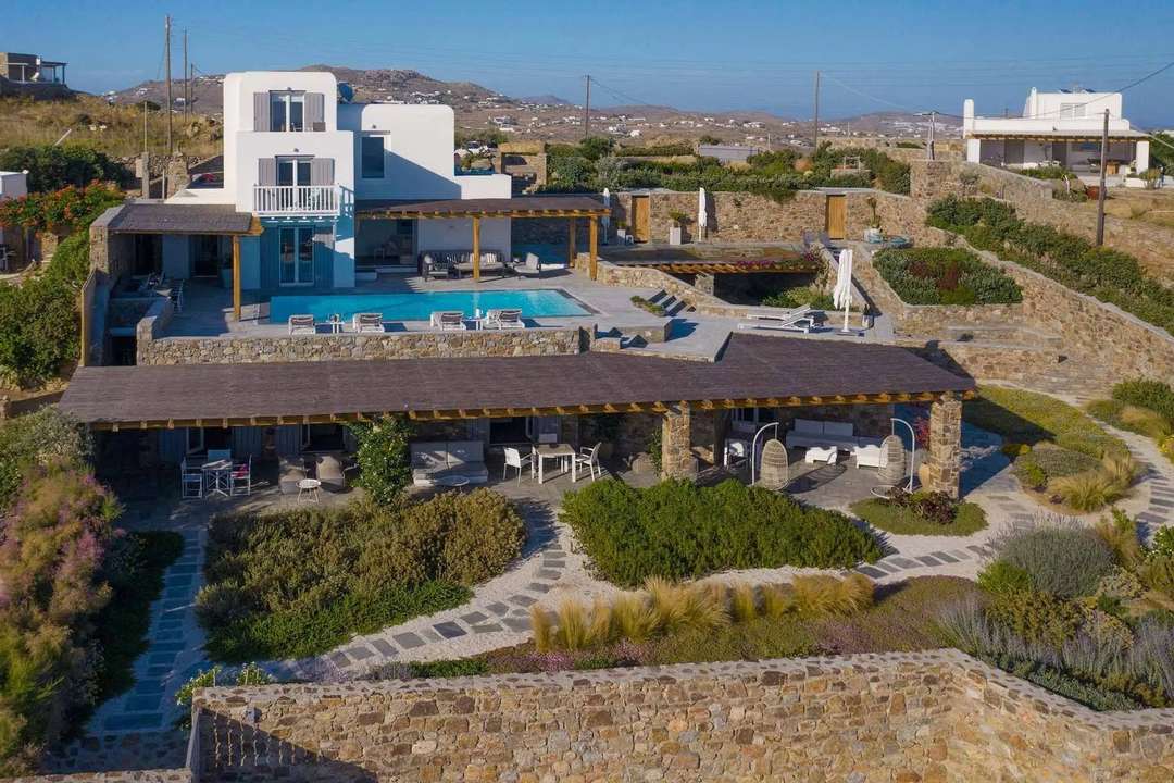 Aerial view of Villa Olivia in Mykonos, featuring a private pool, stone terraces, and panoramic sea views.