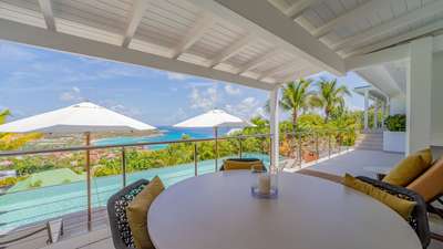 Elegant outdoor lounge on a private villa terrace, featuring a dining table, sun lounger, and stunning Caribbean ocean views.