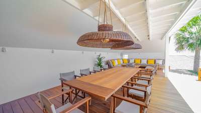 Elegant covered outdoor lounge and dining area with a wooden table, woven lighting, and comfortable seating in St-Barths.
