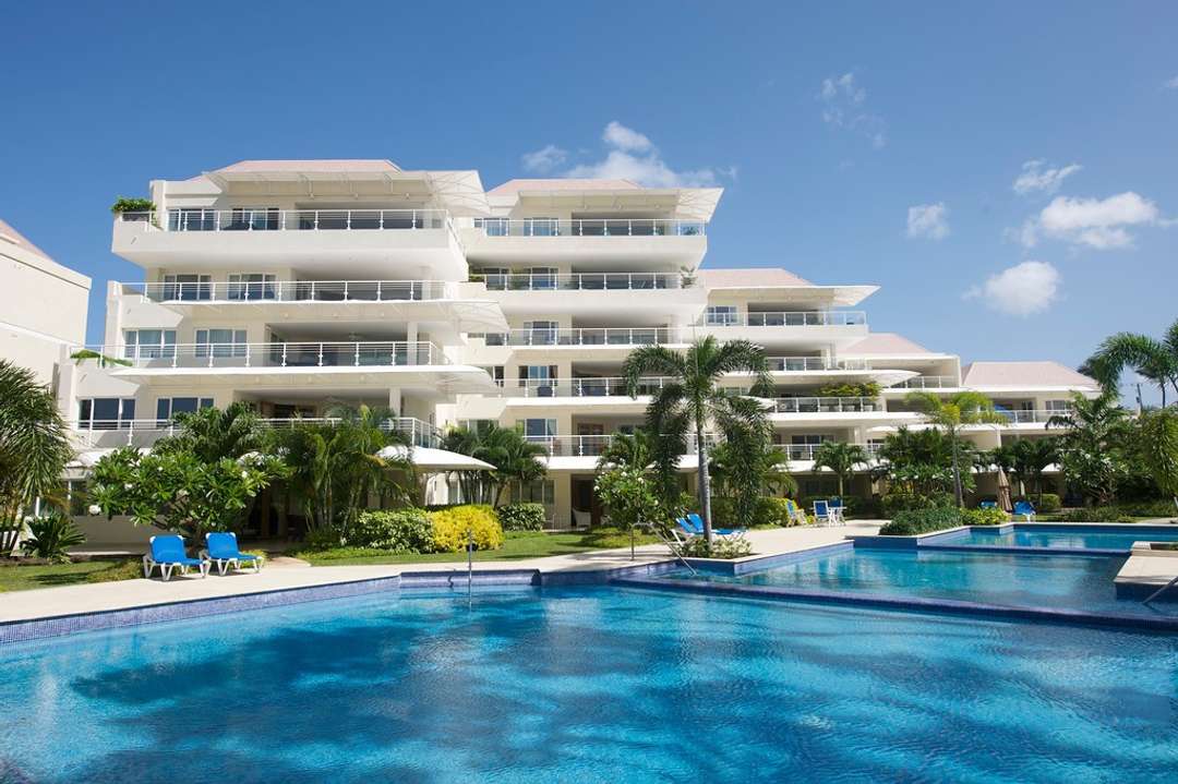 Modern beachfront complex in Barbados featuring a large communal swimming pool, landscaped gardens, and luxury apartments.