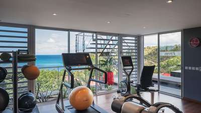 Fully equipped fitness room featuring modern exercise machines, hydro jet massage bed, and floor-to-ceiling ocean views.
