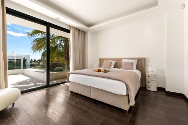 Luxurious bedroom at Paraiso Aurora featuring dark wood floors and floor-to-ceiling glass doors opening to a private terrace.