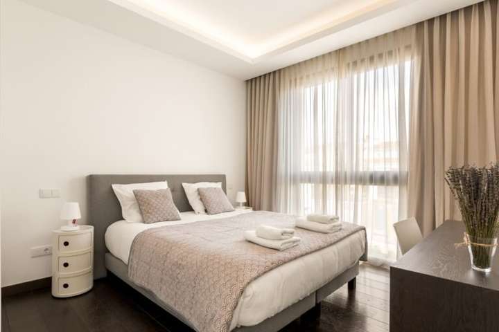 Elegant contemporary bedroom at Paraiso Aurora featuring dark wood floors, a plush bed, and sheer curtains for natural light.