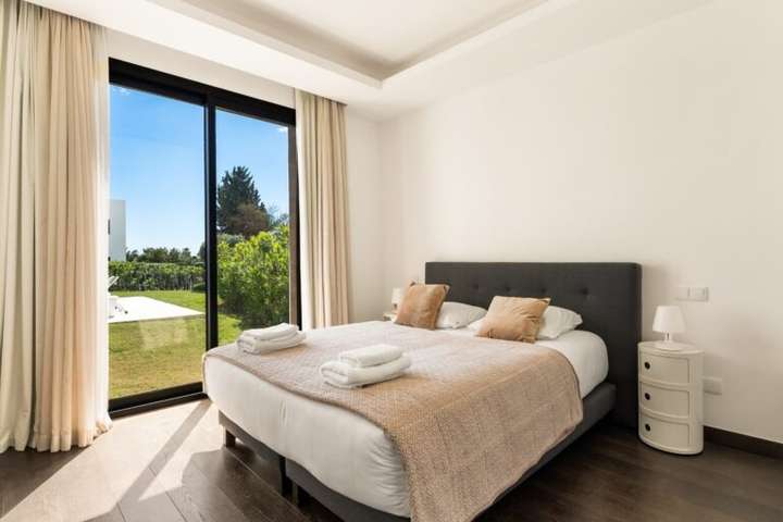 Elegant ground-floor bedroom featuring dark wood flooring, a plush bed, and floor-to-ceiling doors opening to the garden.