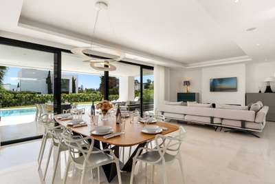 Open-plan dining area featuring a wooden table, modern chandelier, and floor-to-ceiling glass doors opening to the pool.