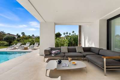 Elegant covered terrace with grey lounge seating and marble floors, overlooking the private pool and lush landscaped gardens.