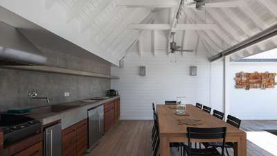 Sophisticated outdoor kitchen and dining space with polished concrete, rich wood accents, and a soaring whitewashed ceiling.
