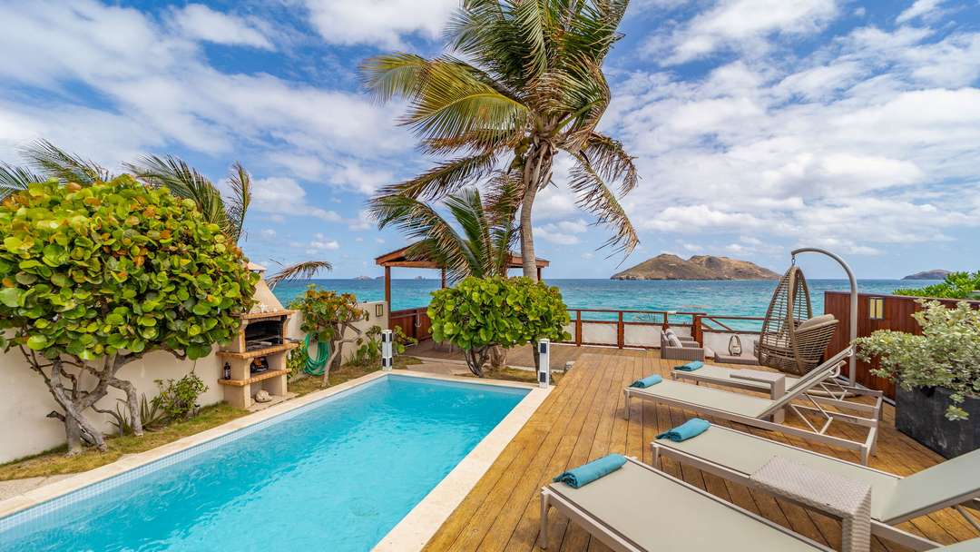 Oceanfront terrace at Villa Raisiniers with a private pool, wooden deck, sun loungers, and stunning Flamands Beach views.