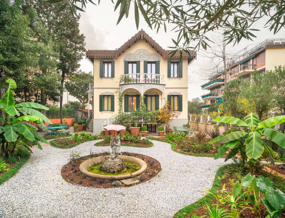Elegant Liberty-style Venice villa exterior featuring a private garden with white pebbles, lush greenery, and a stone fountain.
