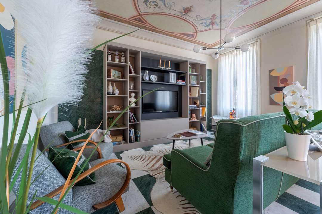 Elegant living room in Florence villa Rena featuring a 1950s aesthetic, green velvet sofa, and stunning frescoed ceiling.