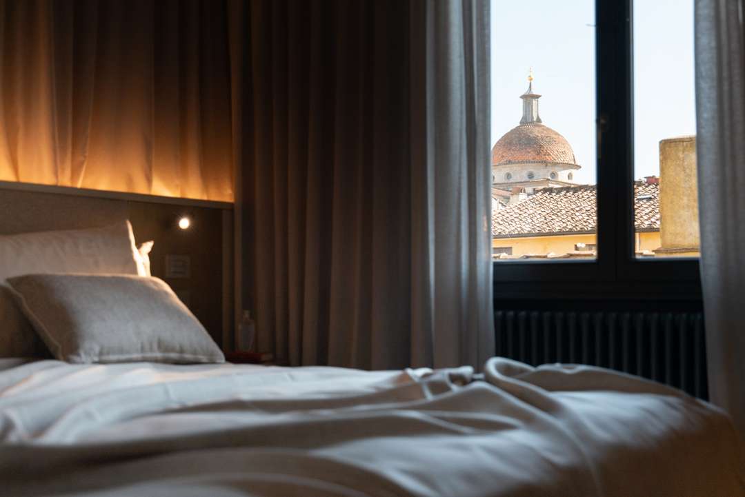 Elegant primary suite in Florence featuring a king-sized bed and a window framing historic Renaissance architecture views.