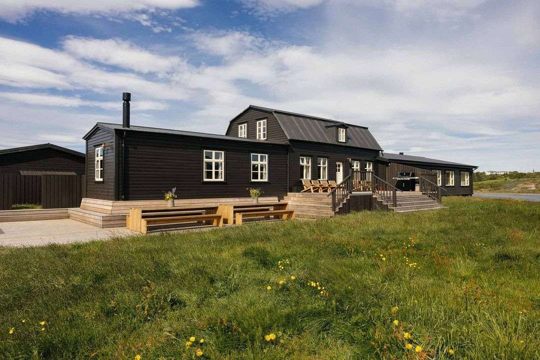 Historic Saga Lodge exterior featuring black wood siding, a spacious wooden terrace, and scenic Icelandic nature views.