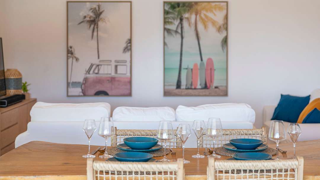 Elegant wooden dining table in a serene St. Barts villa living area, featuring plush white seating and tropical artwork.