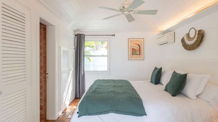Tranquil air-conditioned bedroom with a plush king bed, elegant white wood-paneled walls, and classic terracotta floor tiles.