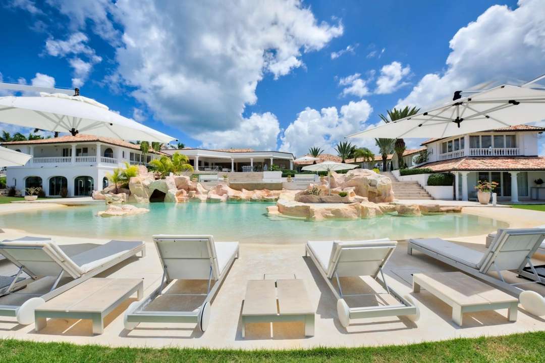 Villa Sandyline's cascading beachfront-style pool with white loungers and sun umbrellas, offering a luxurious tropical escape.