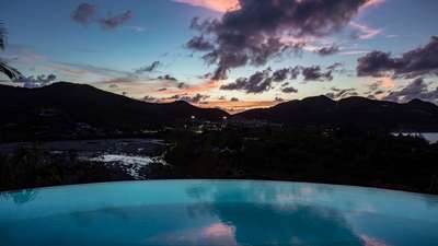 Stunning heated infinity pool reflecting a vibrant sunset sky, offering breathtaking panoramic views of St-Jean Bay.