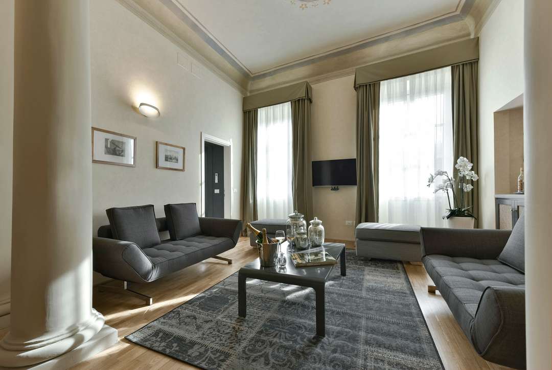 Elegant Florence apartment living room with original frescoed ceilings, classical columns, and minimalist gray sofas.