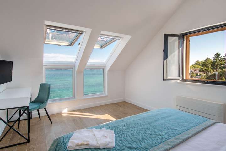 Top-floor king bedroom featuring skylights with stunning Adriatic Sea views, a modern desk, and elegant coastal decor.