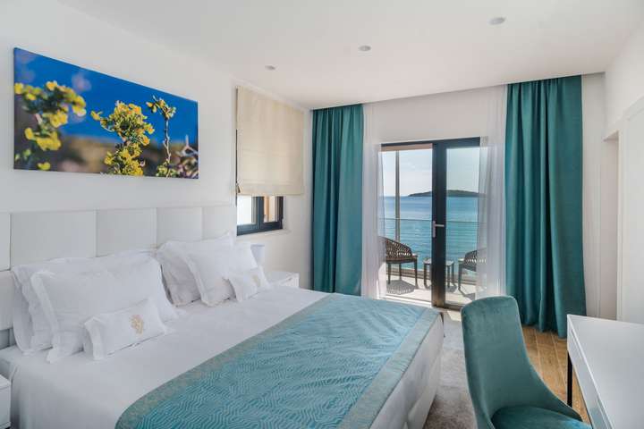 Luxury king bedroom with elegant teal accents and glass doors opening to a private balcony with stunning Adriatic Sea views.