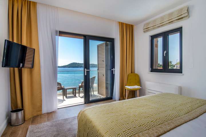 Luxurious master suite with a plush king bed, gold accents, and glass doors opening to a private beachfront balcony.