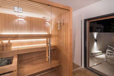 Inside the high-end private sauna featuring warm wood finishes and glass doors opening to the illuminated outdoor terrace.
