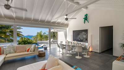 Contemporary living and dining area with an oval table, white sofas, and sliding doors opening to stunning ocean views.
