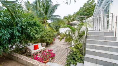 Expansive wooden deck at Villa Skrutten surrounded by lush tropical gardens, vibrant bougainvillea, and tall palm trees.